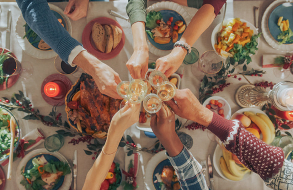 Fentről nézve egy ünnepiesen megterített téli asztal, ahol többen poharat emelnek koccintásra.